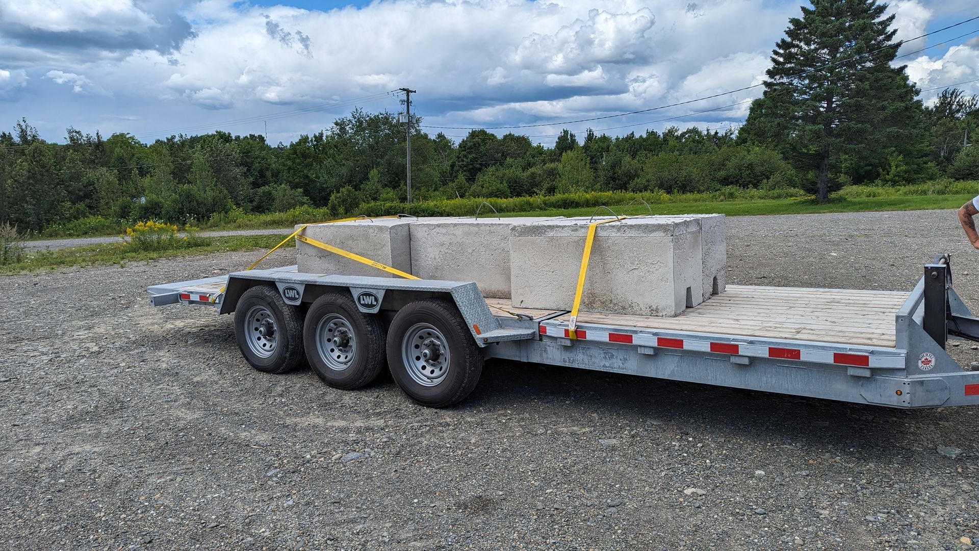 A trailer with concrete blocks on it is parked in a gravel lot.