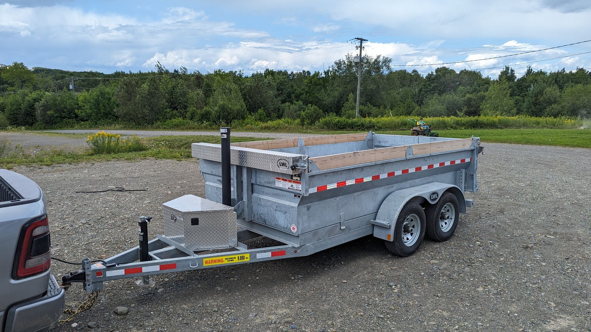 A dump trailer is being towed by a truck in a gravel lot.