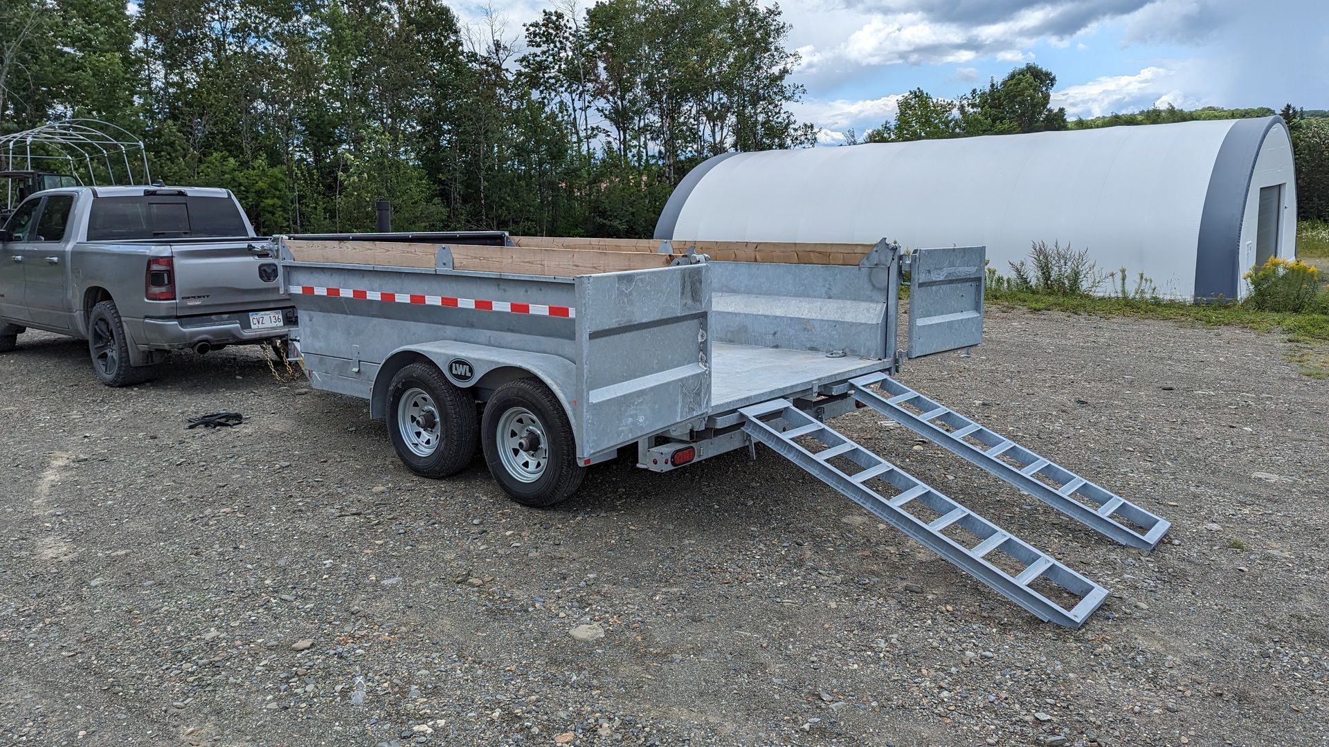 A truck is towing a trailer with ramps in a gravel lot.