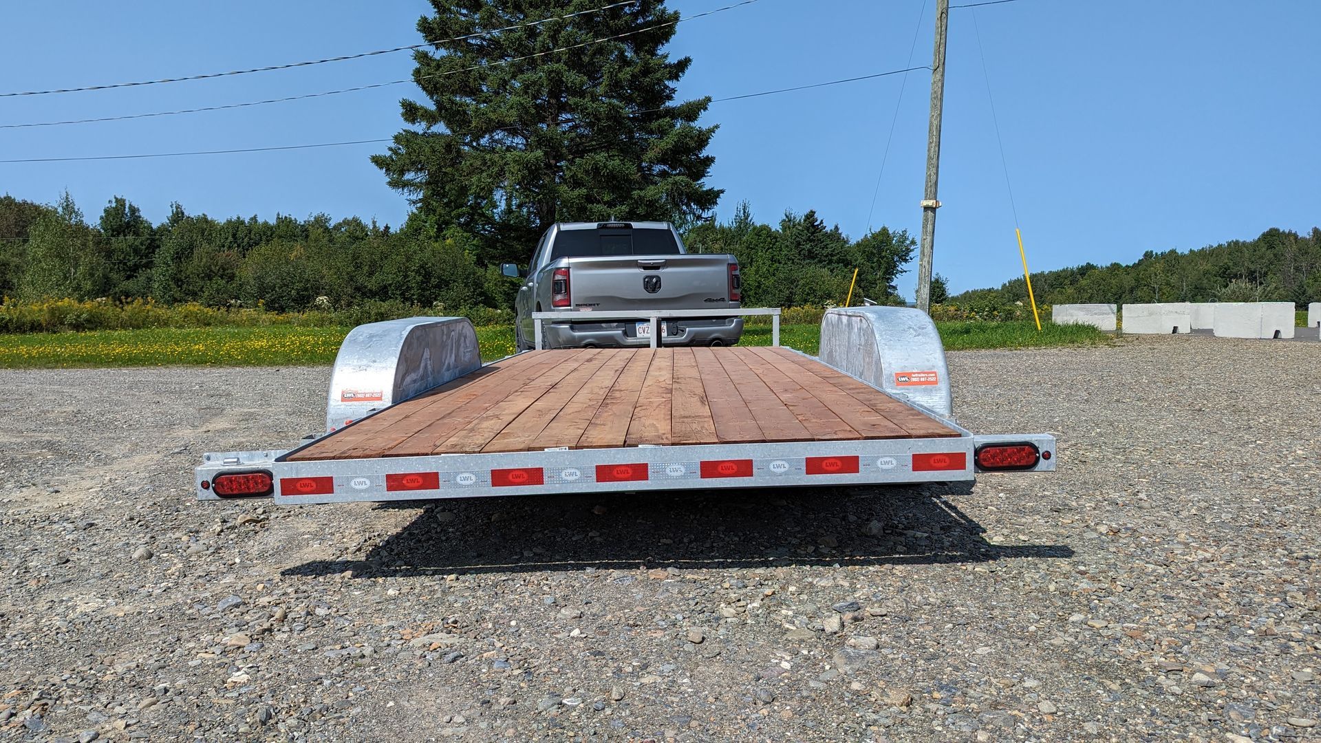 A truck is parked on the back of a trailer in a gravel lot.