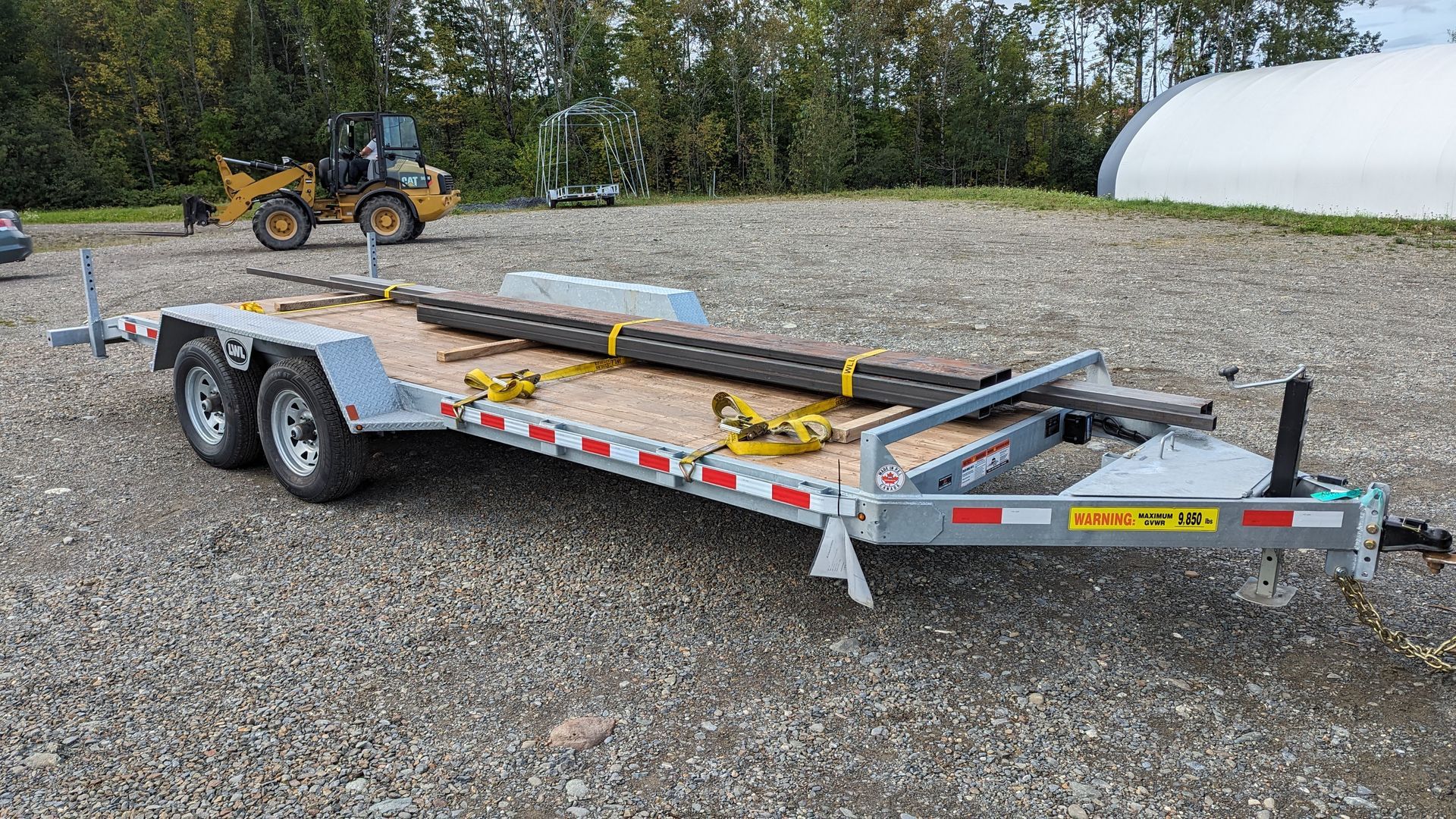 A trailer is parked in a gravel lot next to a tractor.