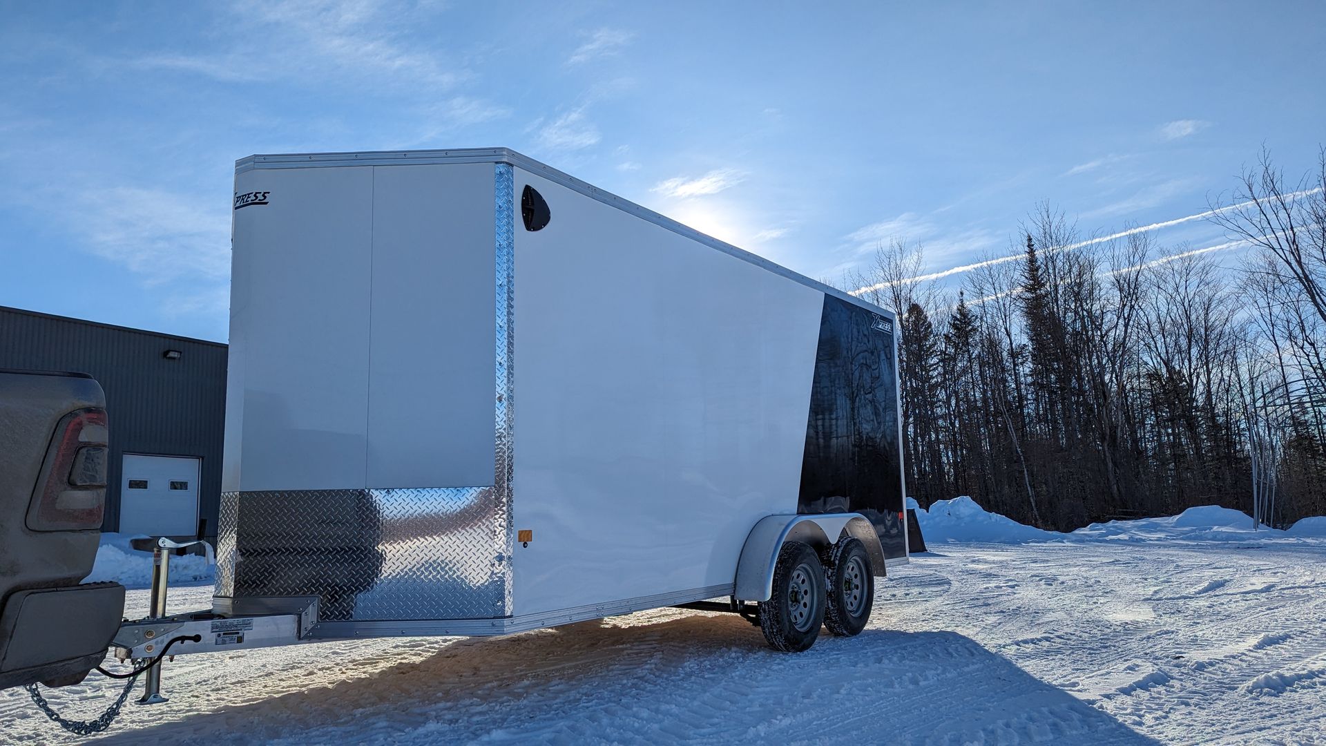 A white trailer is parked in the snow next to a truck.