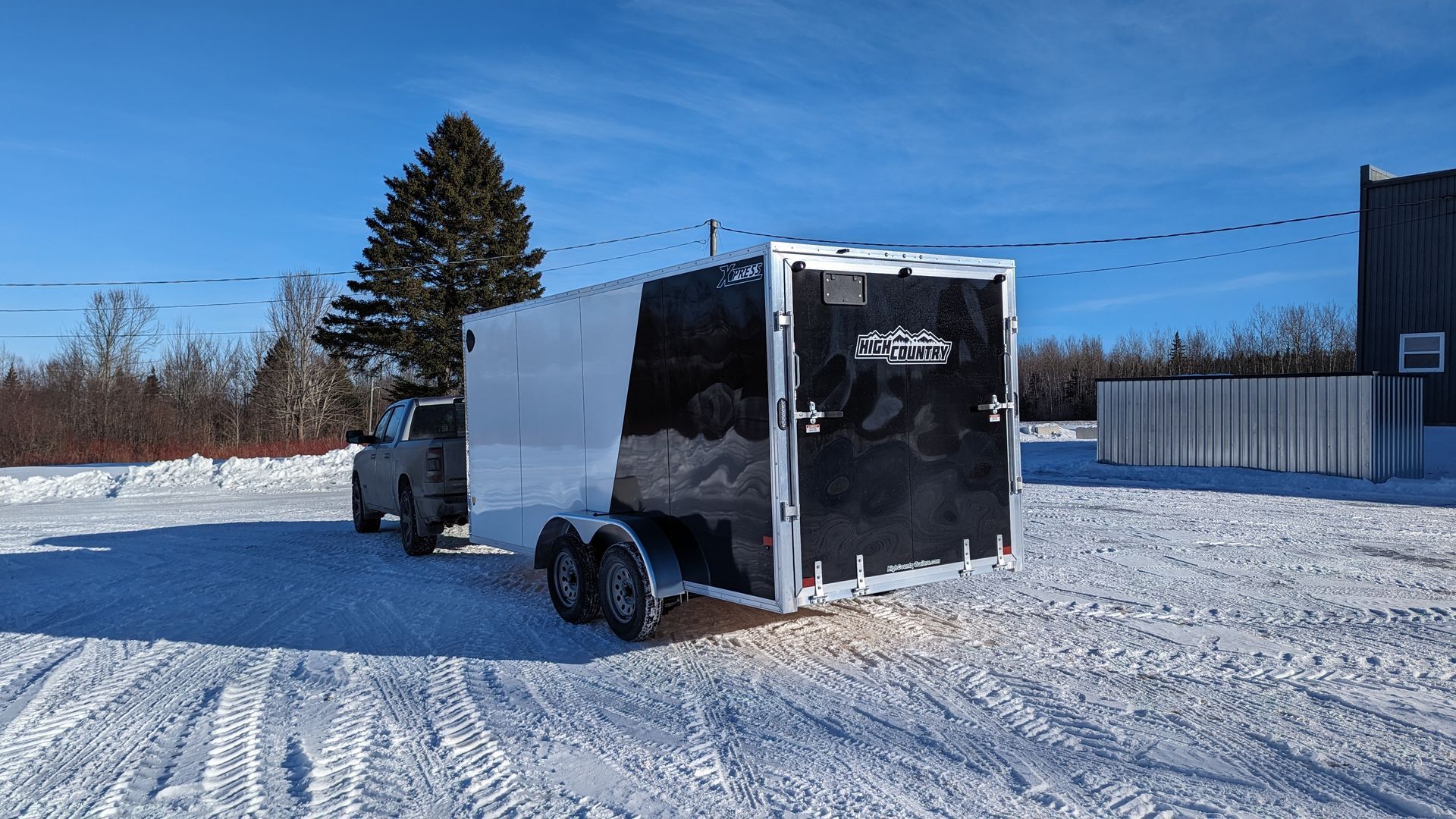 A black and white trailer is parked in the snow next to a truck.