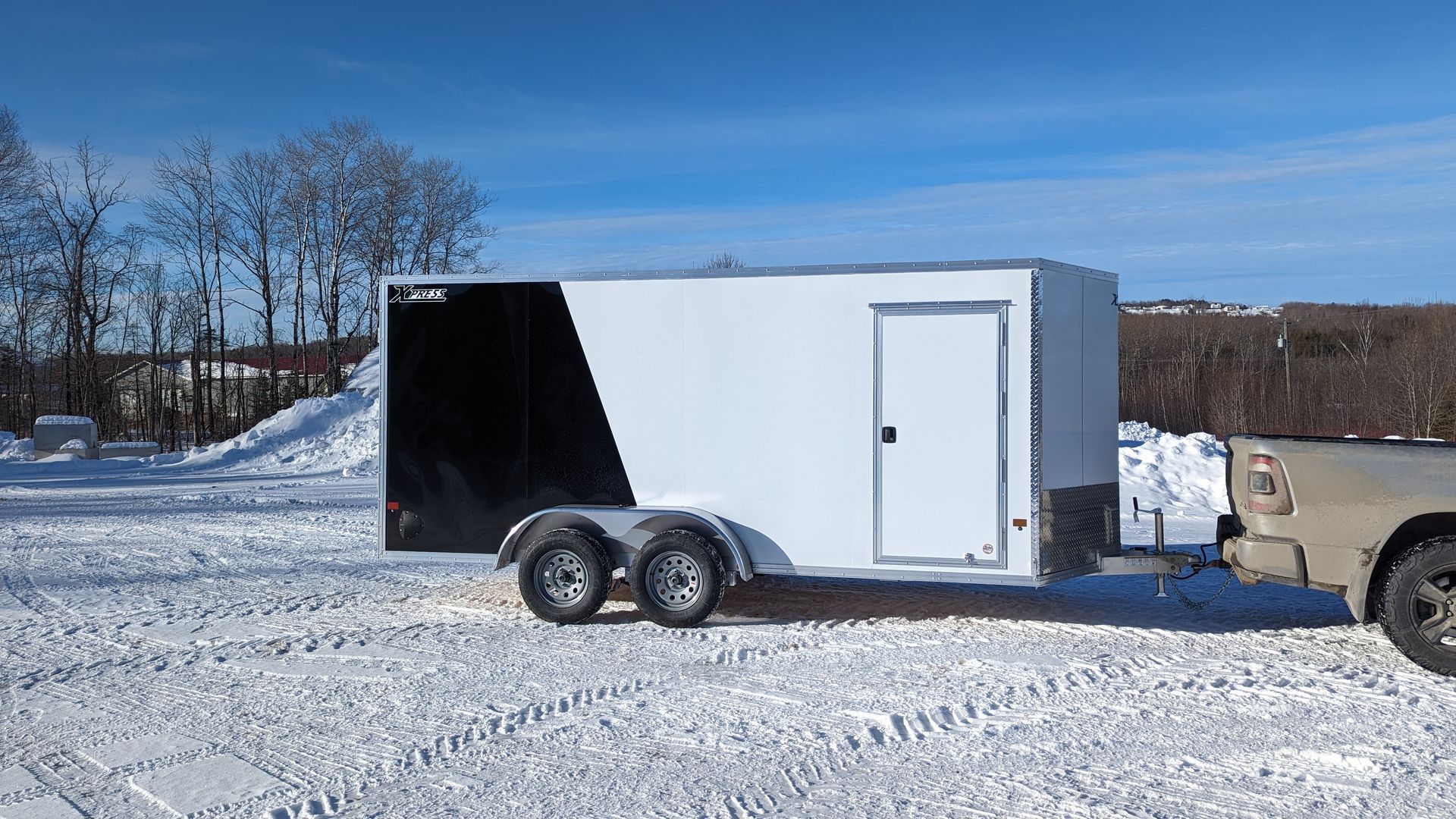 A black and white trailer is being towed by a truck in the snow.