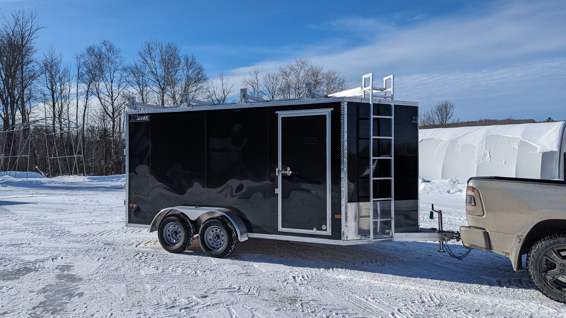A black trailer is being towed by a truck in the snow.