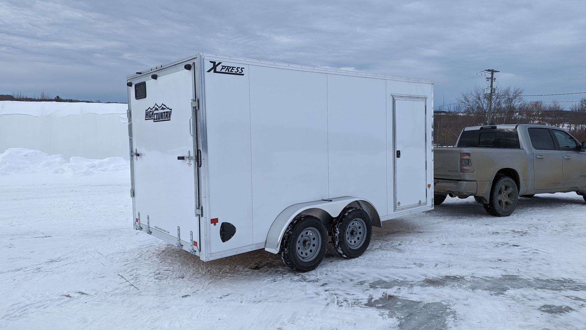 A white trailer is being towed by a truck in the snow.