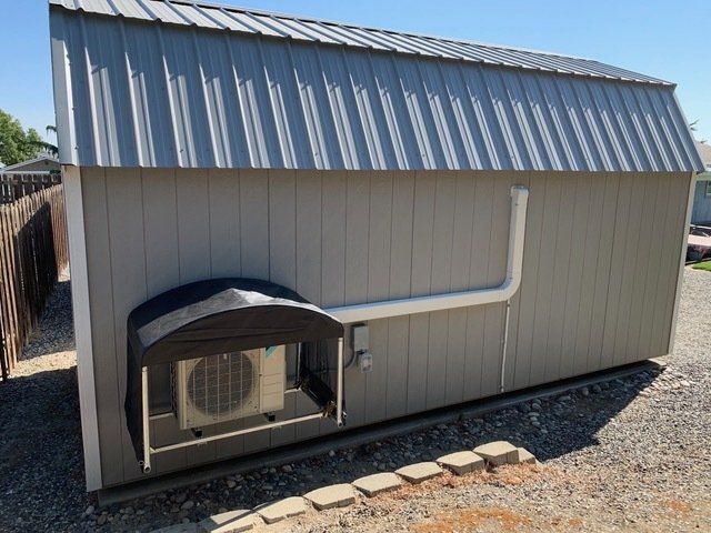 Grey shed with metal roof and attached AC unit.  White exhaust pipe runs to the roof.
