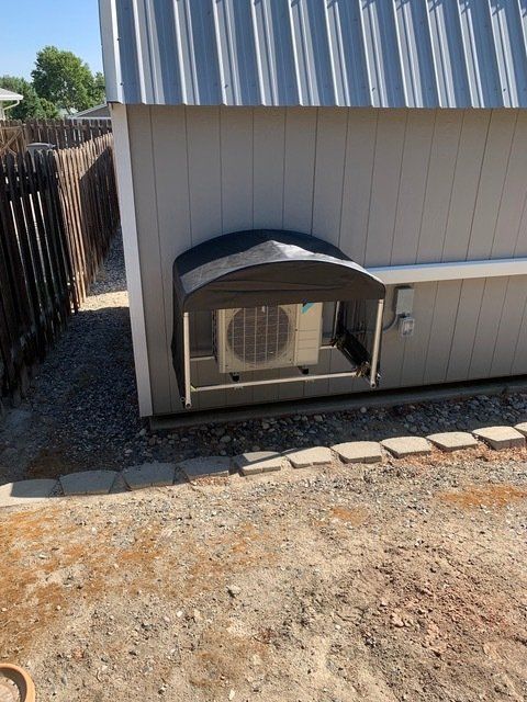 An air conditioner unit installed on the side of a building, covered by a black canopy.