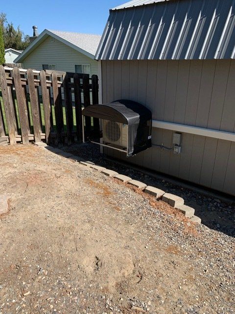 Air conditioner unit on the side of a building, near a wooden fence and gravel.