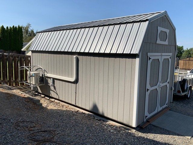 Gray shed with metal roof, white trim, and double doors; an air conditioning unit is attached to the side.