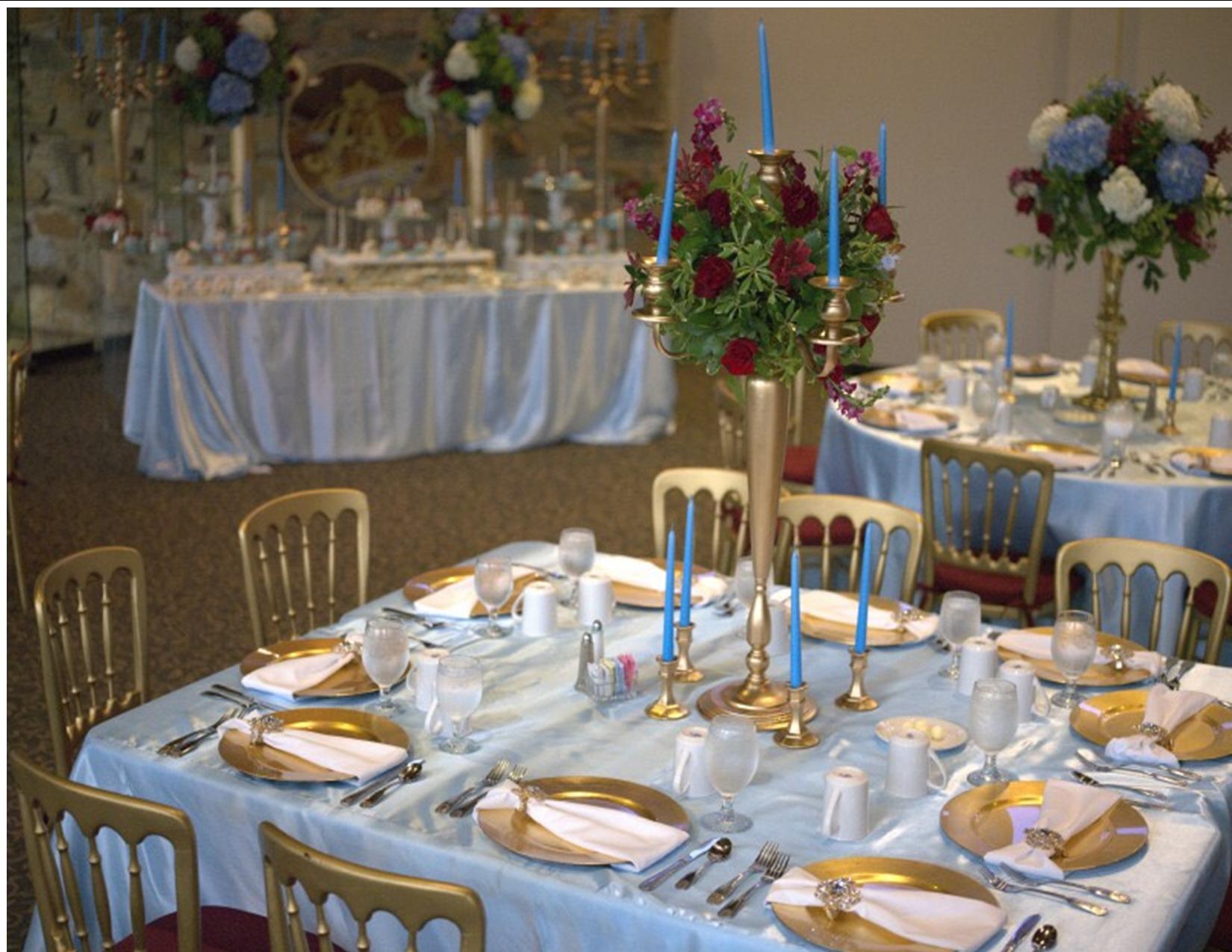 Formal dining tables set with gold chargers, blue tablecloths, and floral centerpieces.