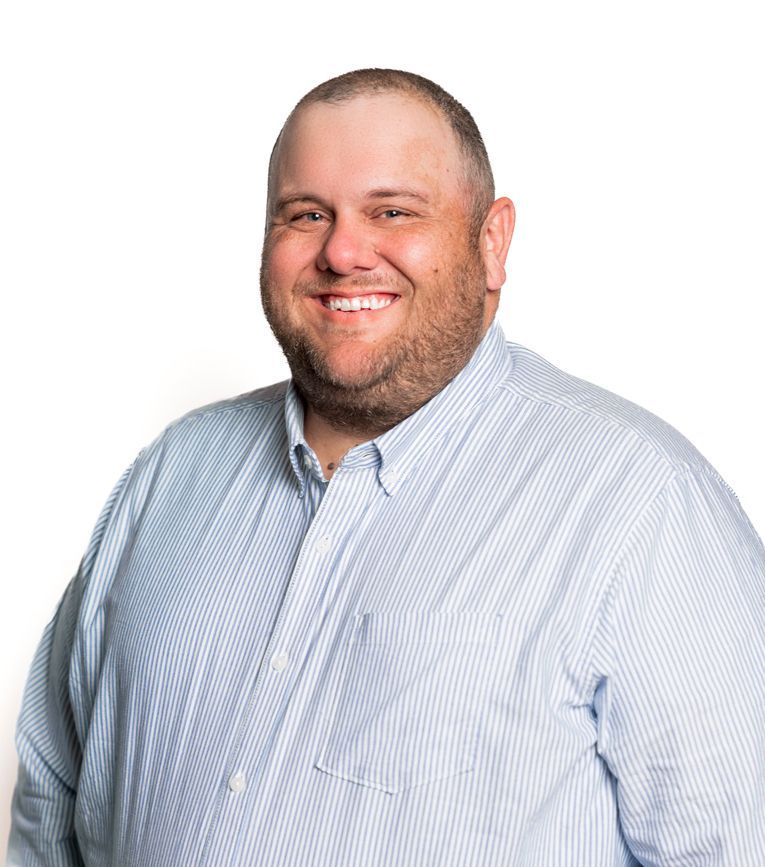 Man with a shaved head and beard smiles while wearing a light blue, button-down shirt.