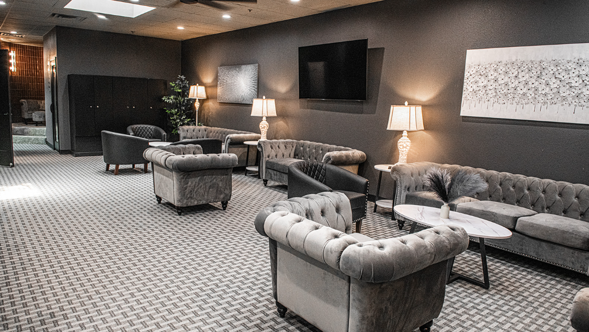 A lounge with gray tufted sofas, armchairs, lamps, and a patterned carpet.
