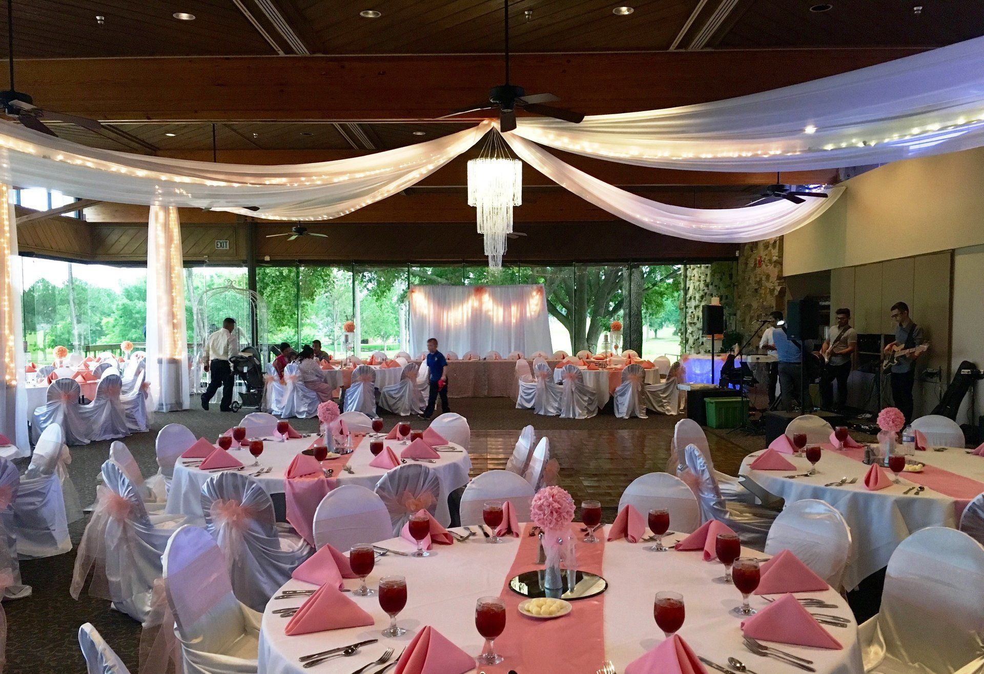 Reception hall decorated for an event with pink and white linens and a band playing in the background.