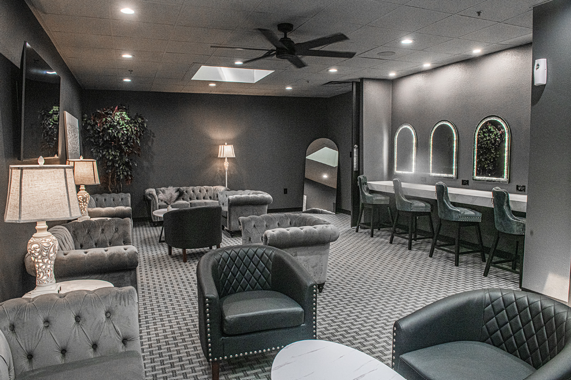 Elegant lounge with seating, mirrors, and vanity area. Dimly lit with dark gray walls.