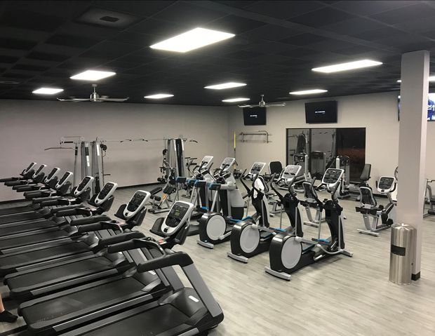 Gym interior with rows of treadmills, elliptical machines, and weight equipment.