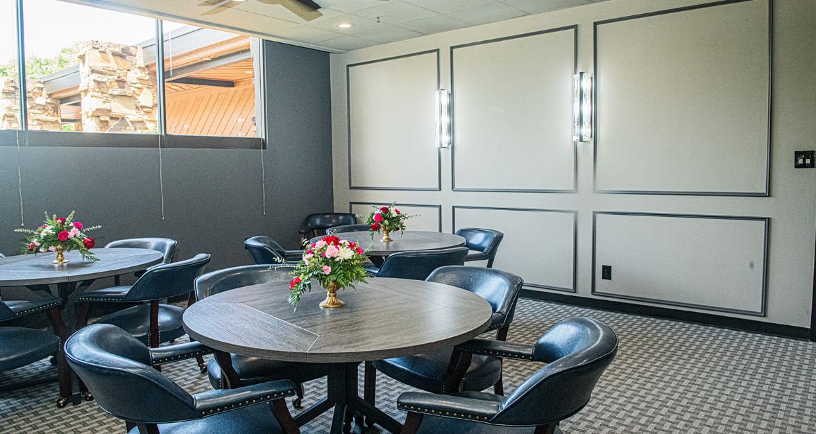 Round tables with flower centerpieces and blue chairs in a room with patterned carpet and paneled walls.