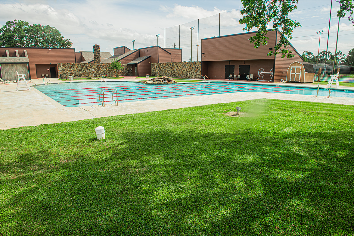 Swimming pool with buildings, surrounded by green grass.