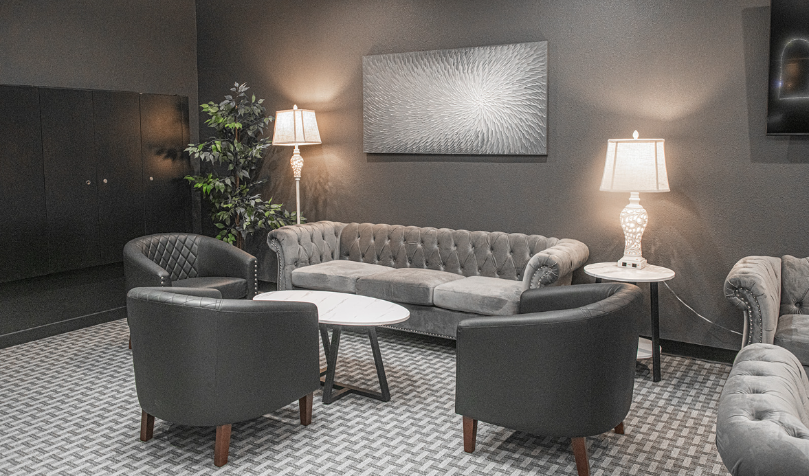 Lounge area with gray sofas, armchairs, small tables, and lamps on a textured rug.
