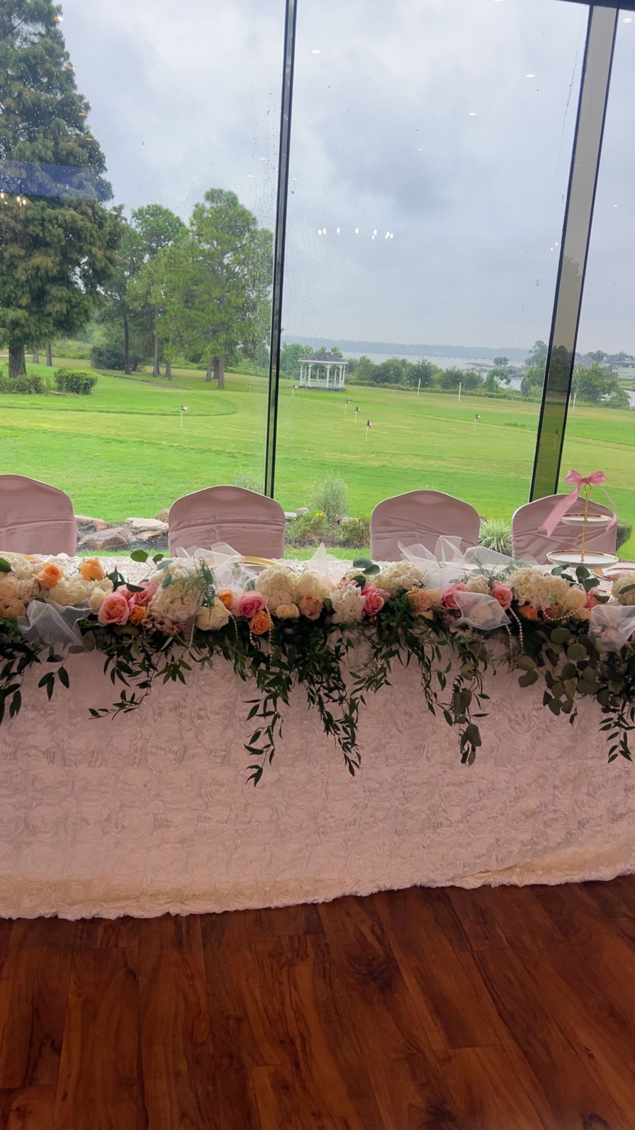 Long table decorated with flowers, in front of a window overlooking a green field.