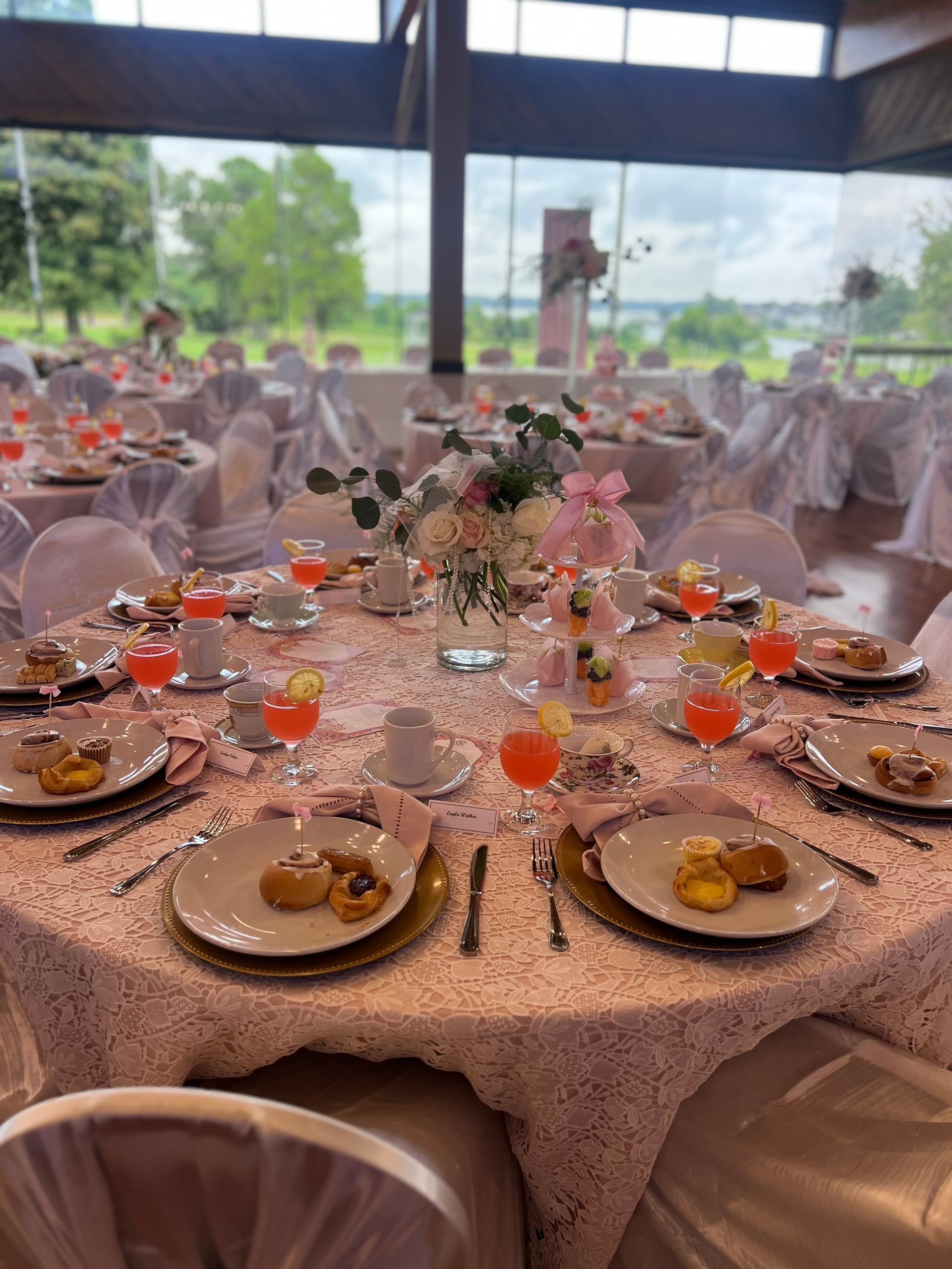 Tables set for an event with floral centerpieces, plates, and drinks, overlooking a view.