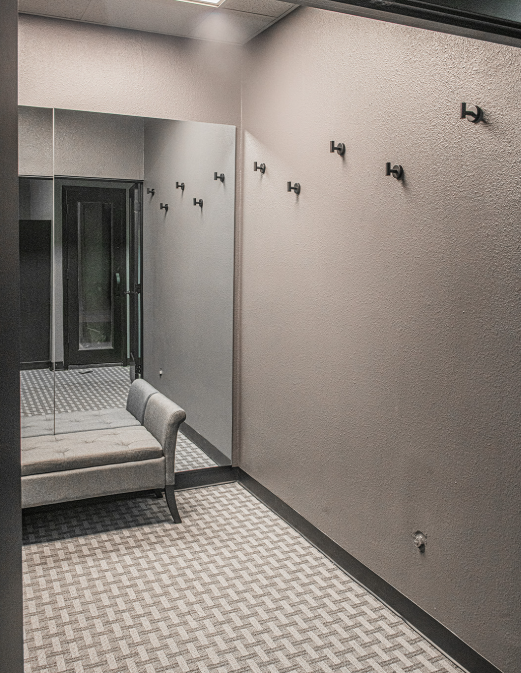 Narrow hallway with mirror, bench, and coat hooks. Gray walls, carpet, and dark door visible.