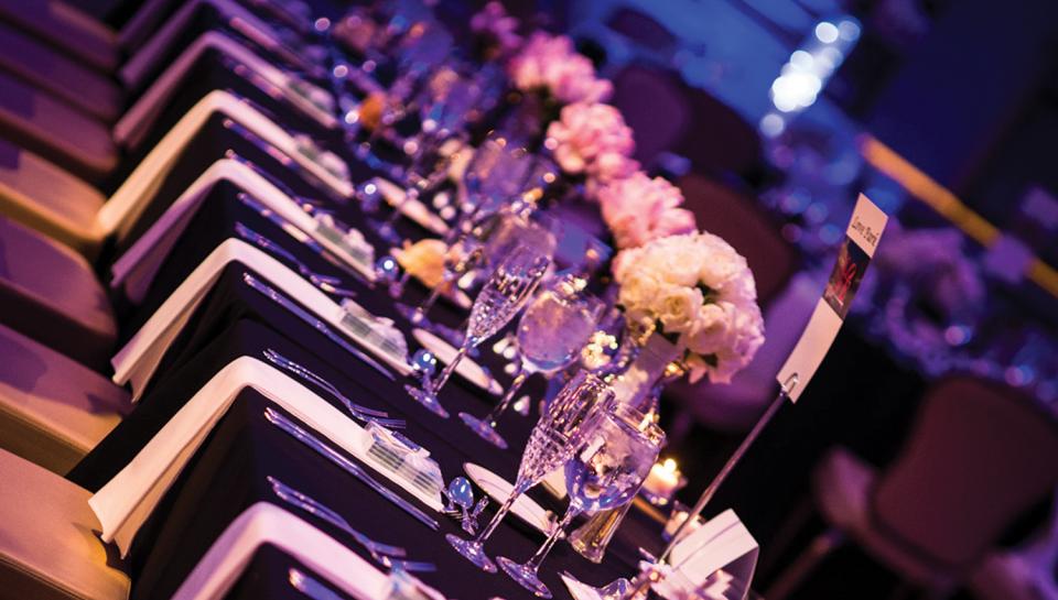 Elegant dinner table setting with black tablecloth, white napkins, floral centerpieces, and champagne glasses.
