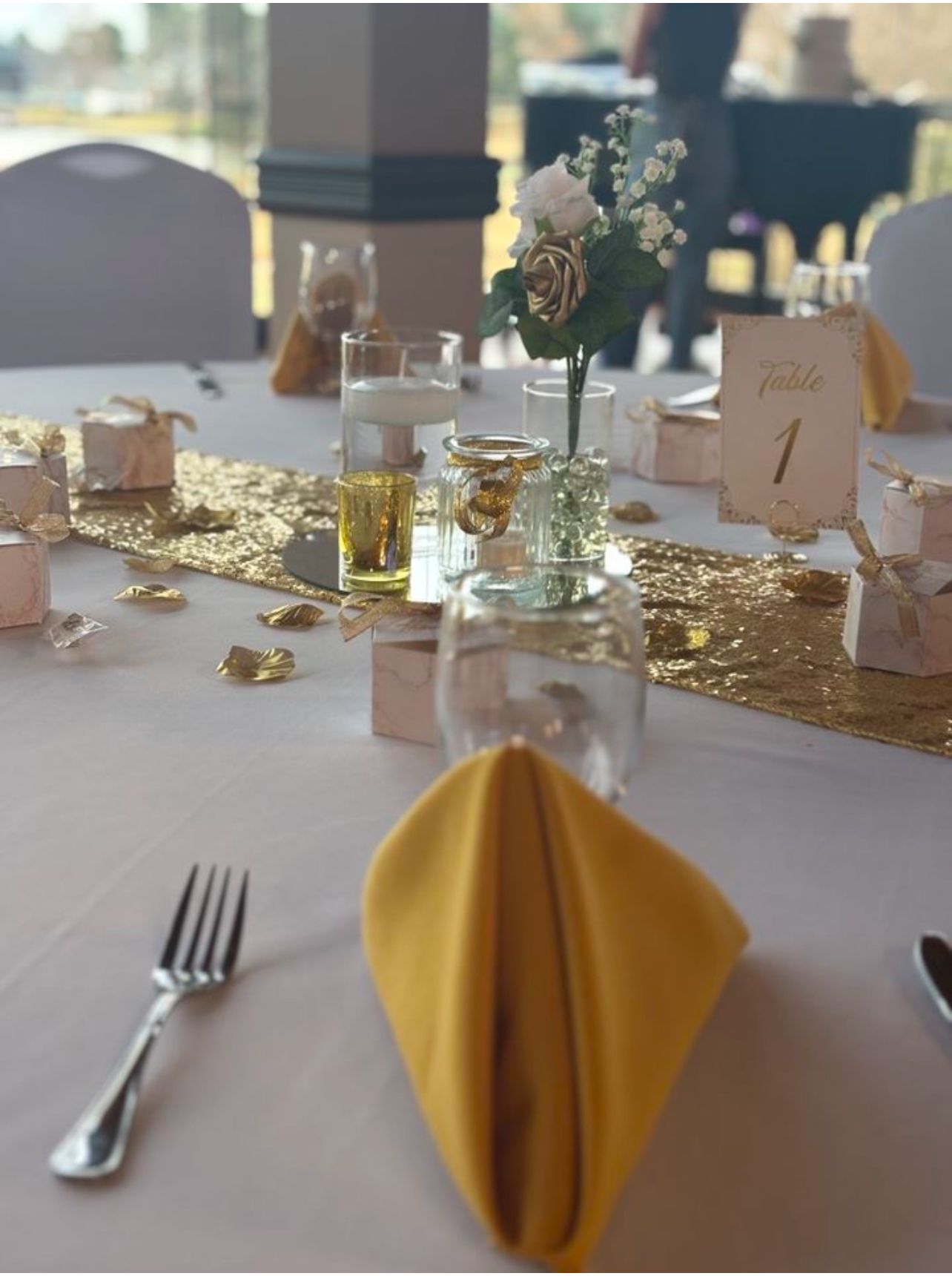 Wedding table setting: gold sequin runner, yellow napkins, small floral arrangement, table number 