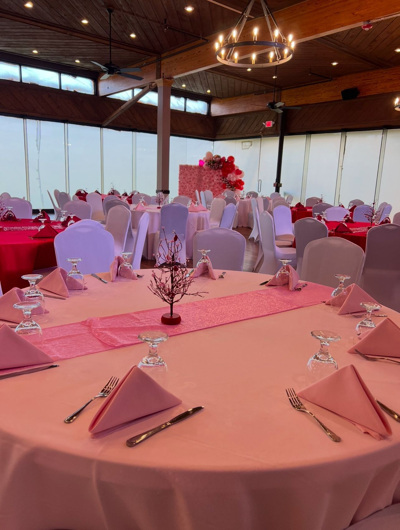 A decorated banquet hall with round tables set for an event; pink linens and napkins.