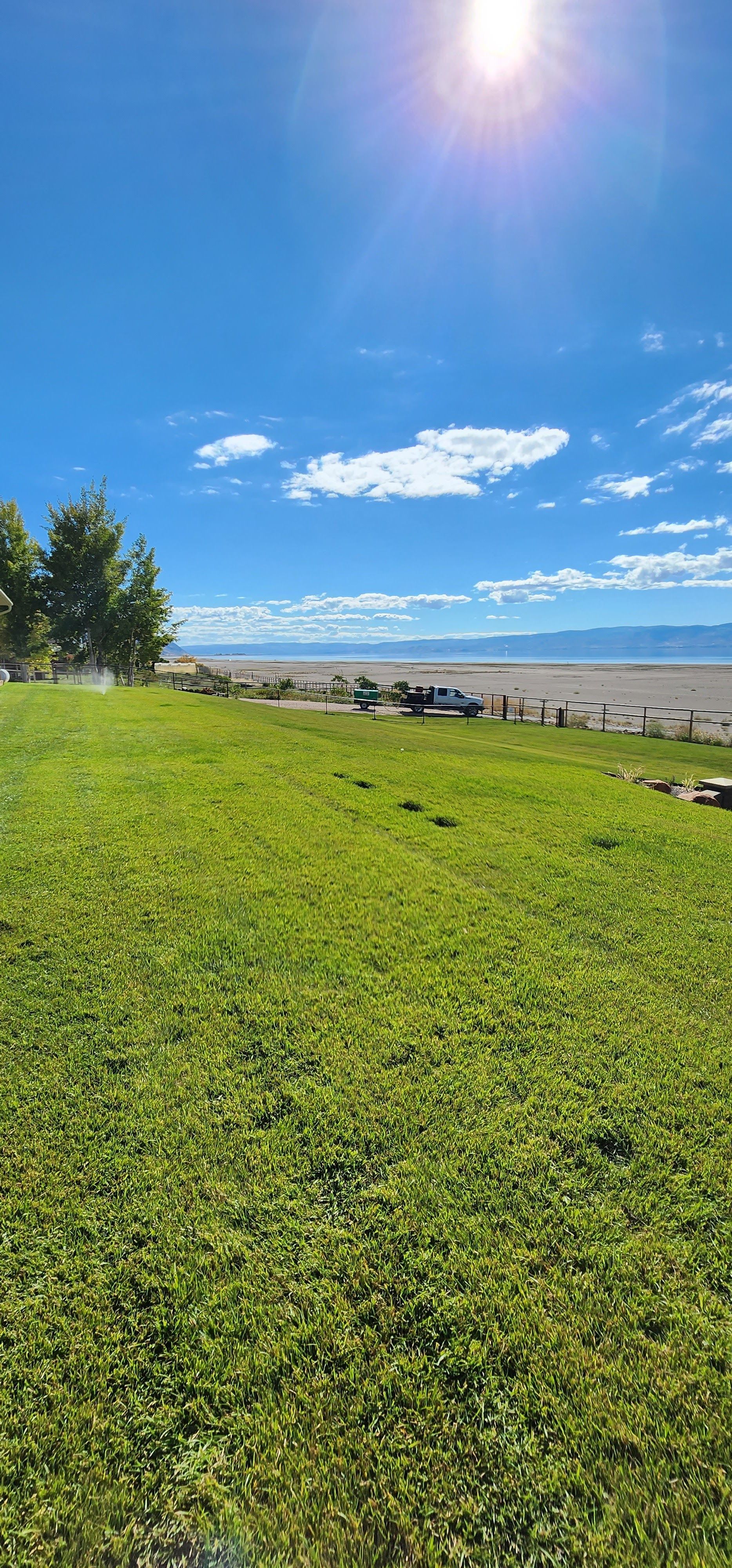 A Large Grassy Field with A Beach in The Background on A Sunny Day.