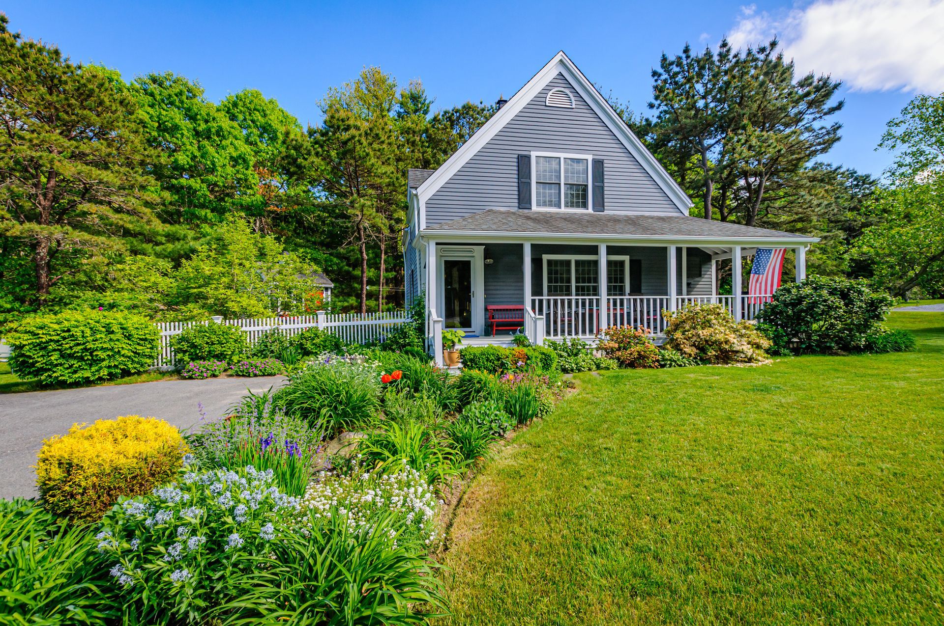A House with A Large Porch and A Lot of Flowers in Front of It.