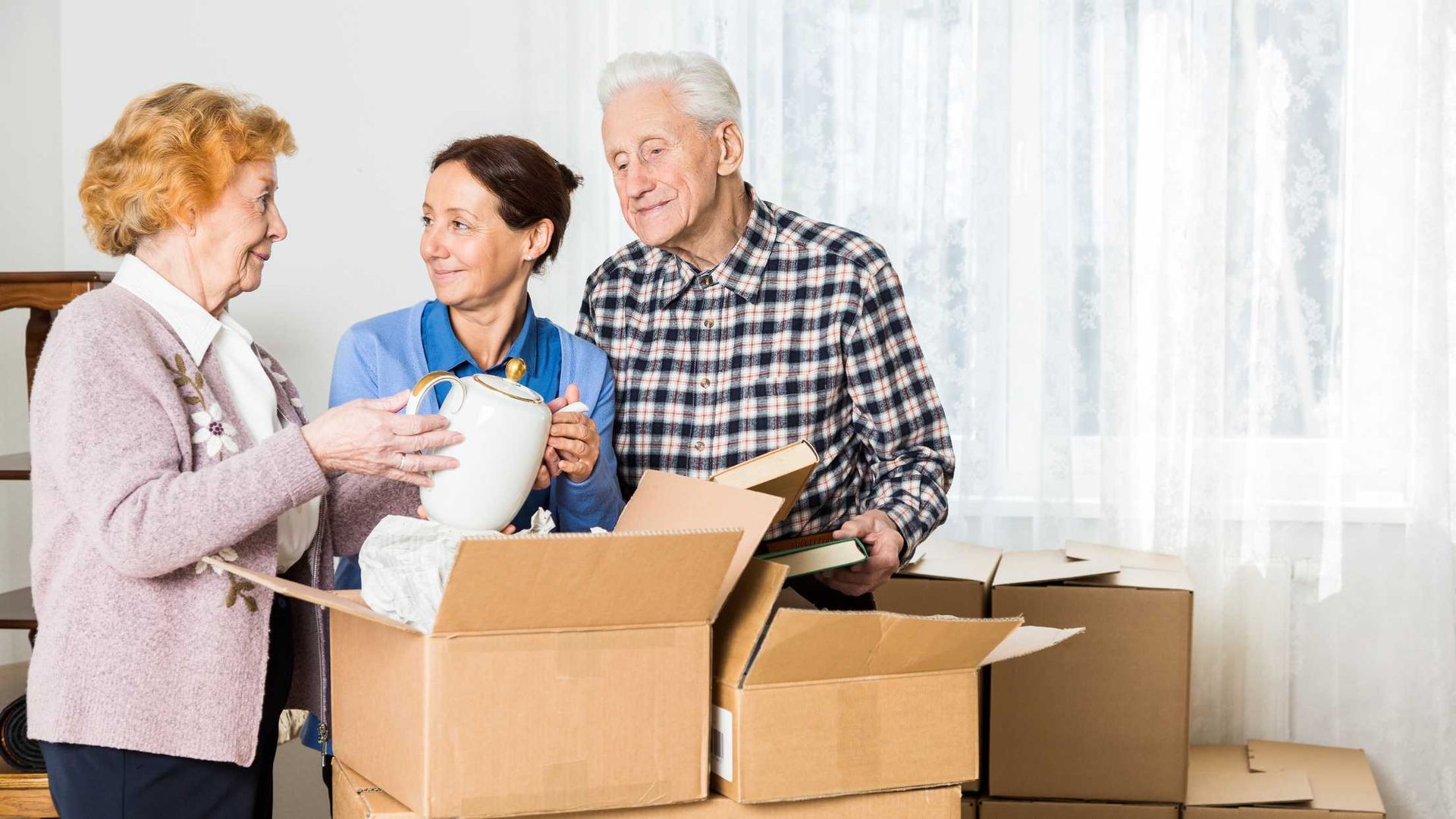 Three people unpacking boxes in a bright room with sheer curtains