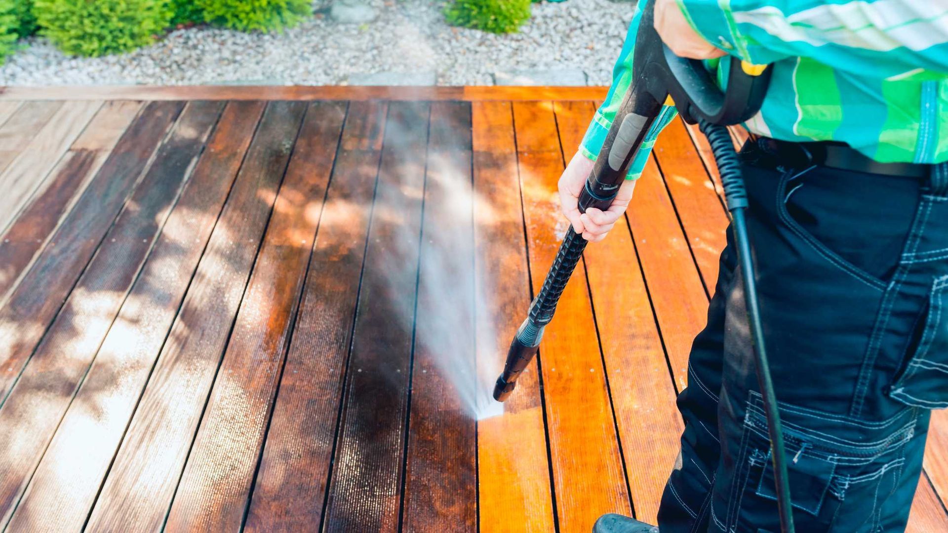 Person pressure-washing a wooden deck, with wet and clean planks visible.