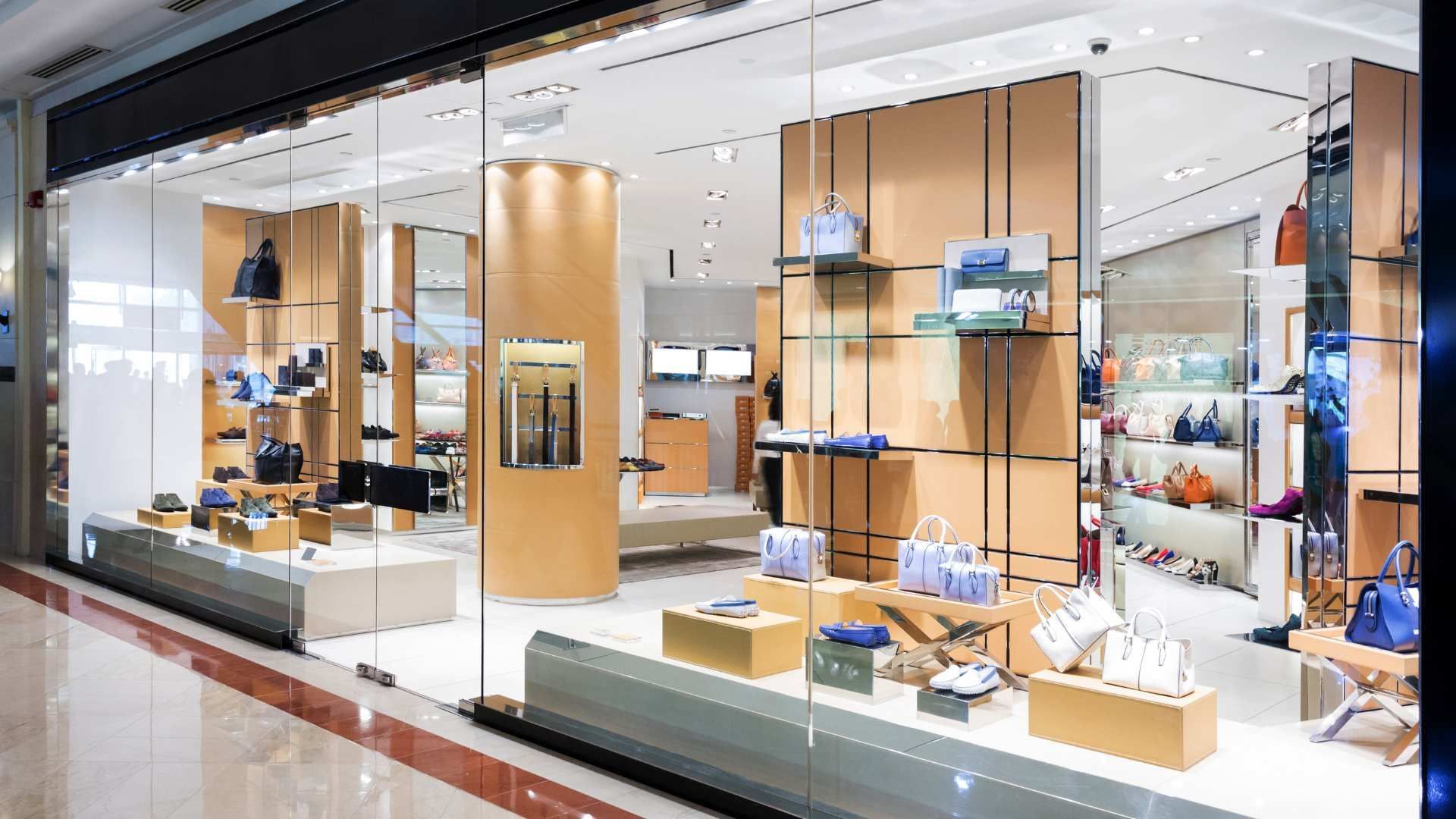 Bright luxury retail store interior with glass displays, wooden shelving, and handbags on display