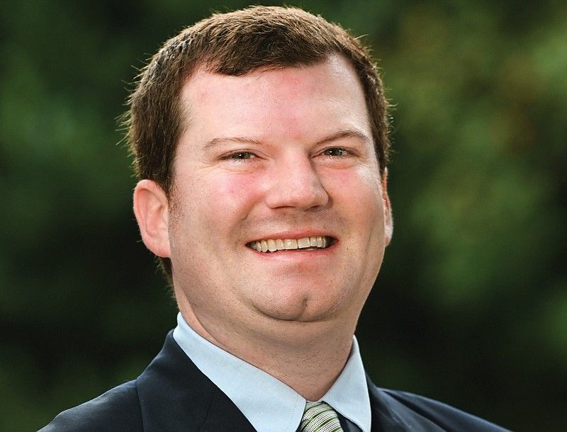 Smiling man in a suit against a blurred green background.