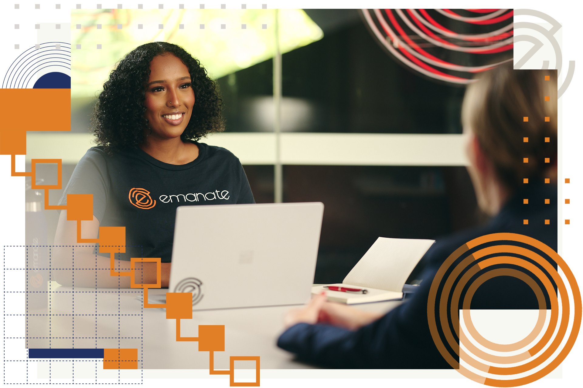 A woman is sitting at a table with a laptop and talking to another woman.