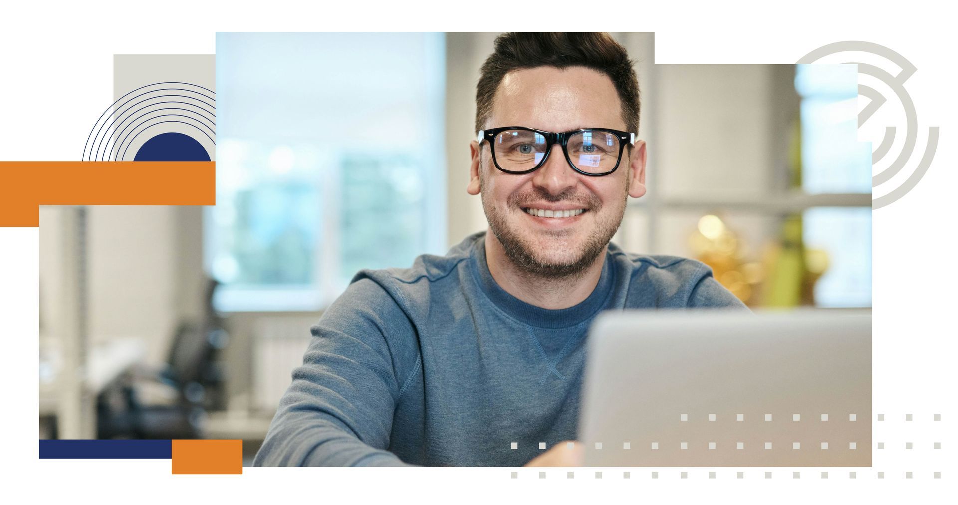 Smiling man with glasses using a laptop in a bright office setting