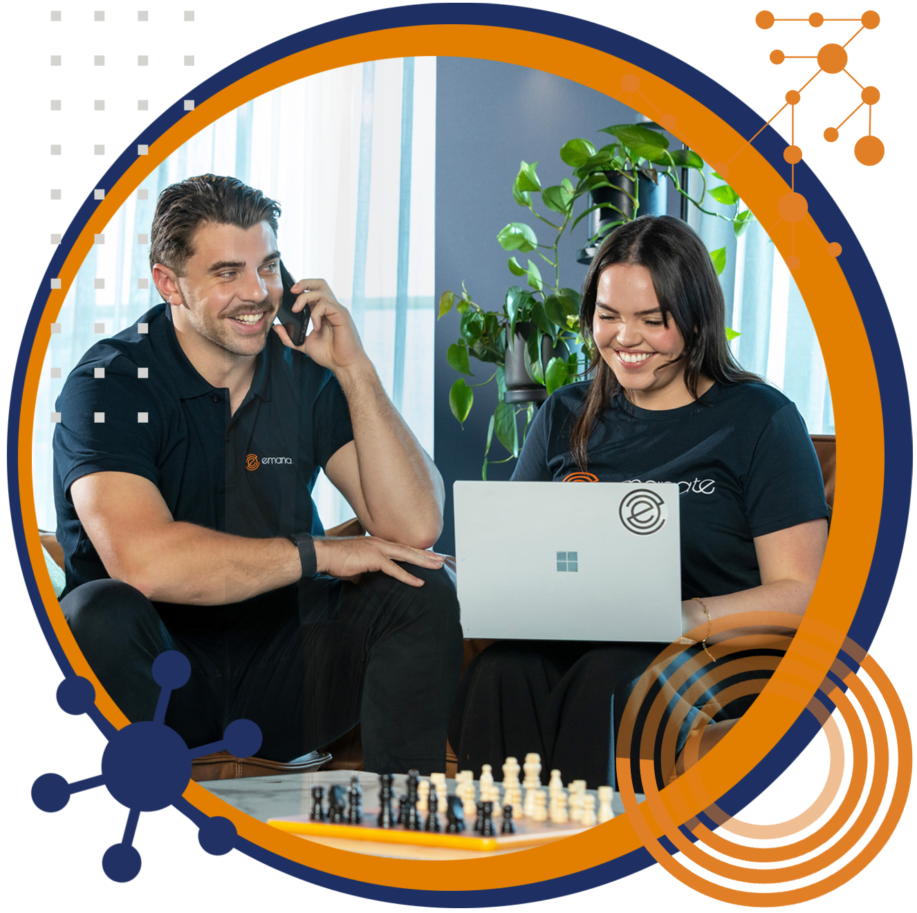 Man on phone and woman using laptop, both smiling, sitting near a chessboard and greenery, inside a circular frame.