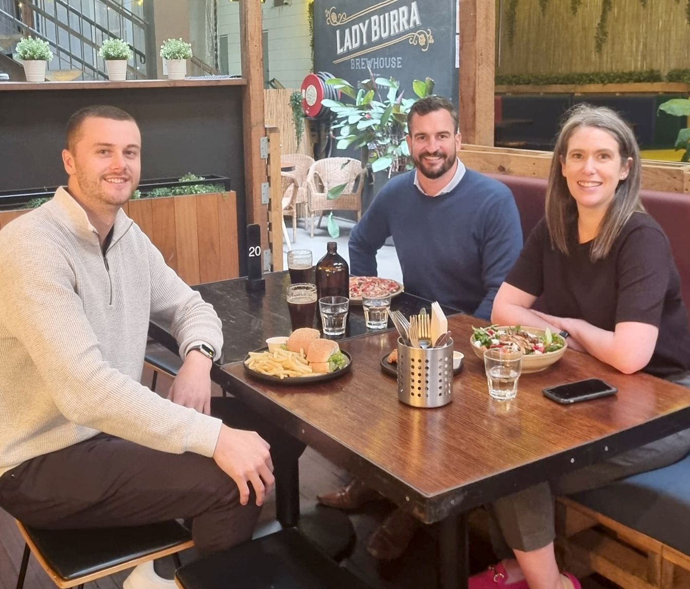 Three people are sitting at a table with food and drinks.