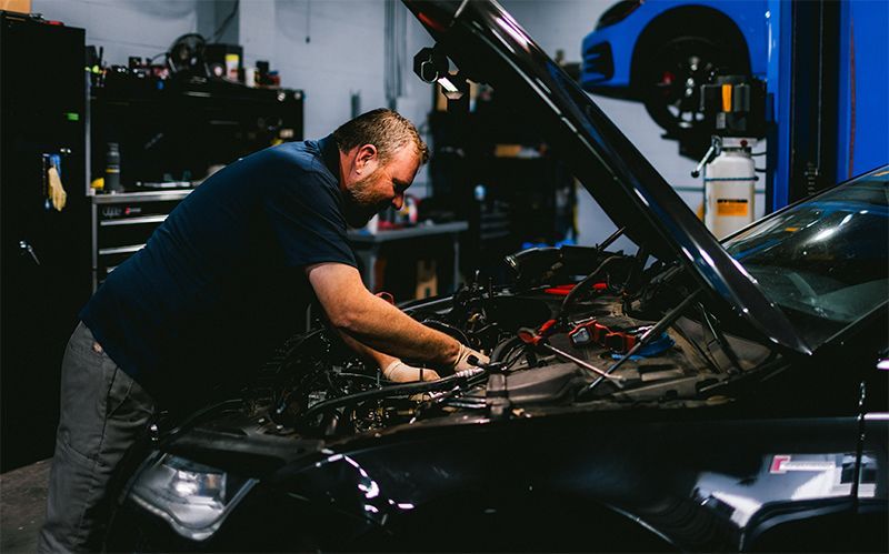 Mechanic working under the hood of a black car in a garage at night