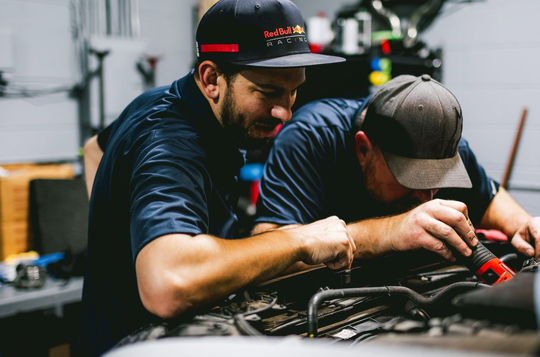 Two mechanics in caps working on a car engine in a garage.