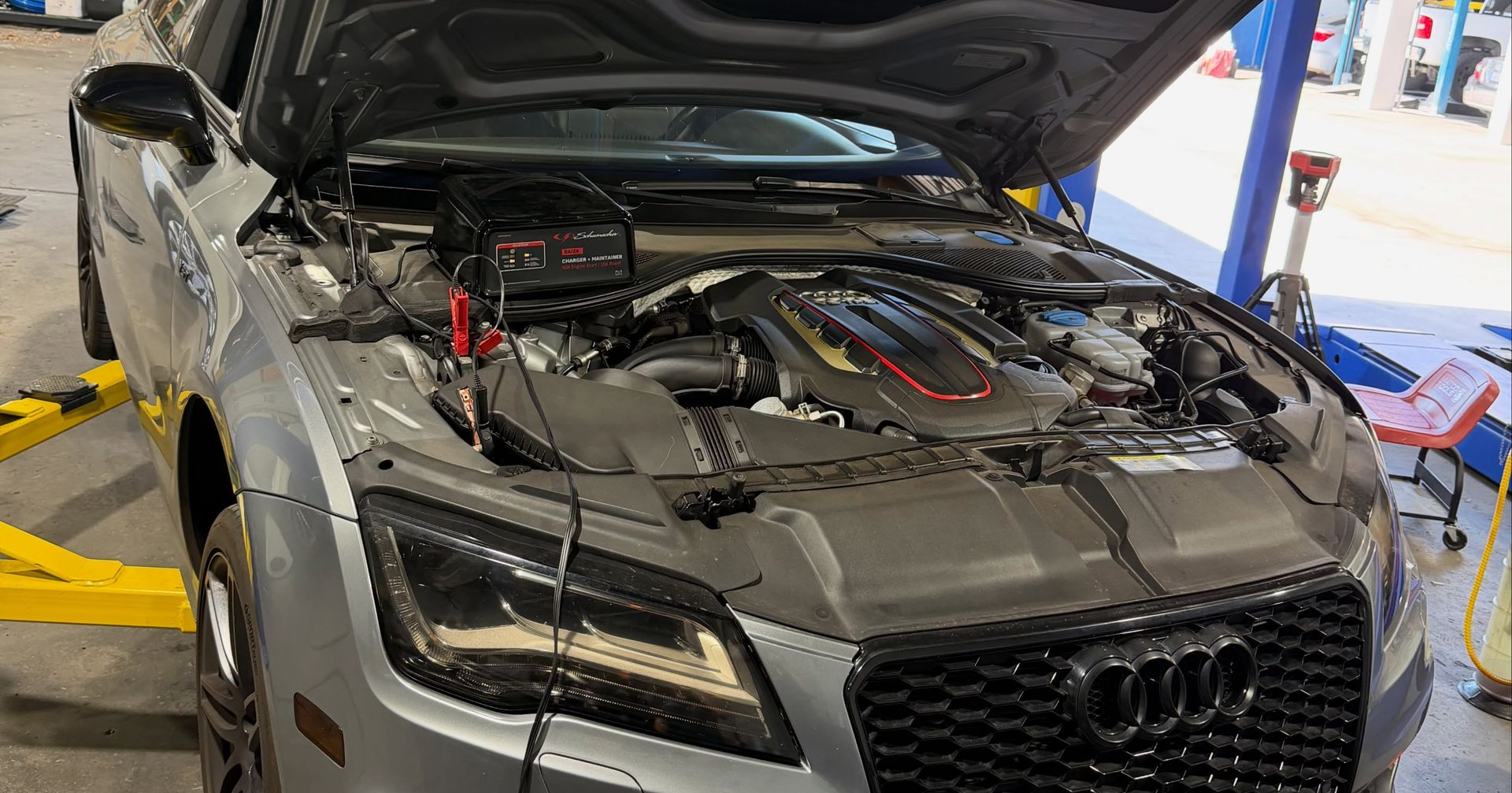 Gray Audi sports car with hood open in a repair shop, engine exposed on a lift.