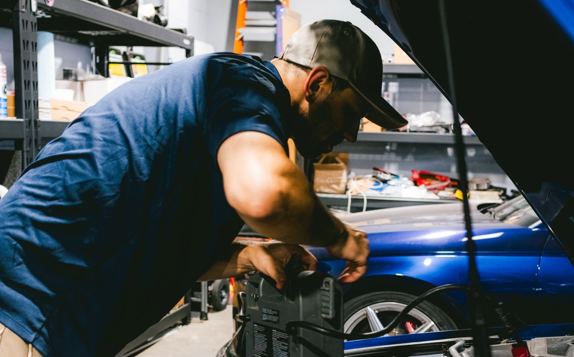 Mechanic working under a blue car in a garage, inspecting engine components.