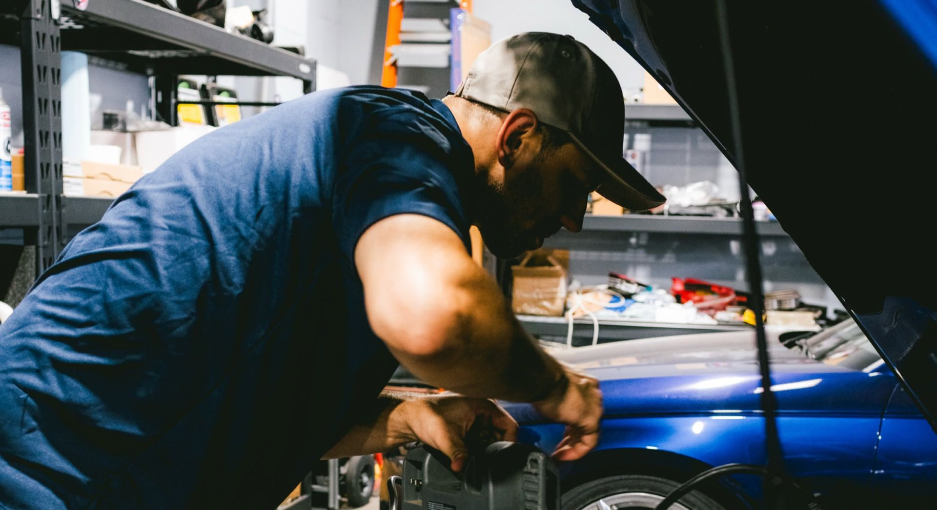 Silver sports sedan in an auto shop, lowered with black rims and a vented hood on a lift.