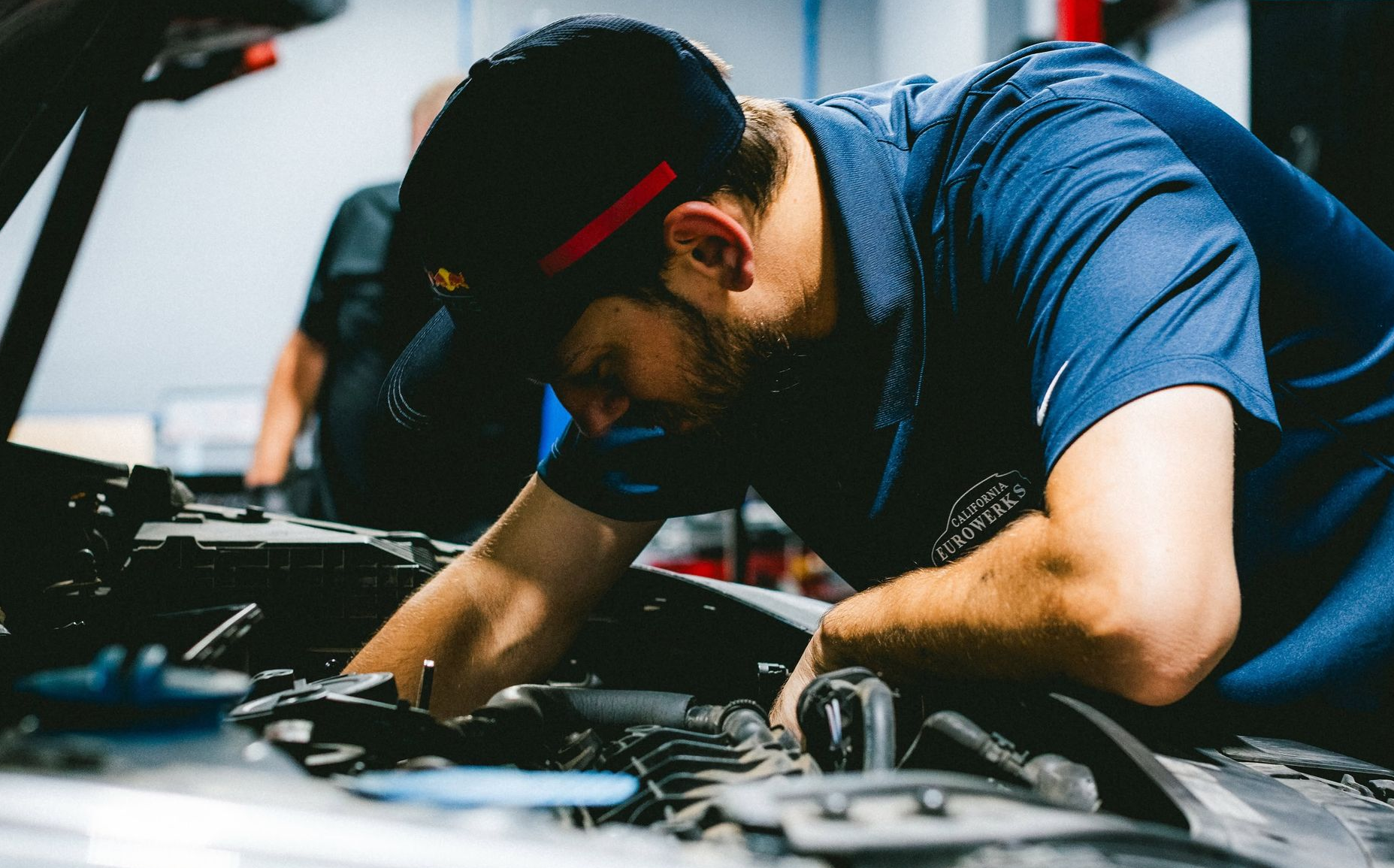 Mechanic in a blue shirt leaning over an open car engine, working in a garage