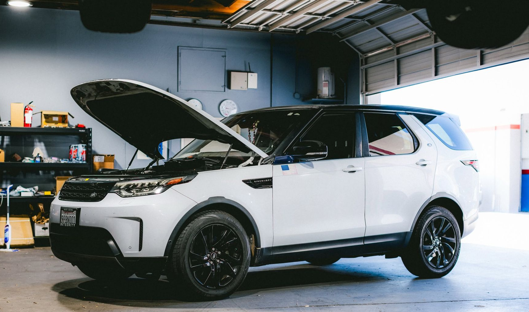 White SUV with hood open in a garage, likely being repaired or inspected