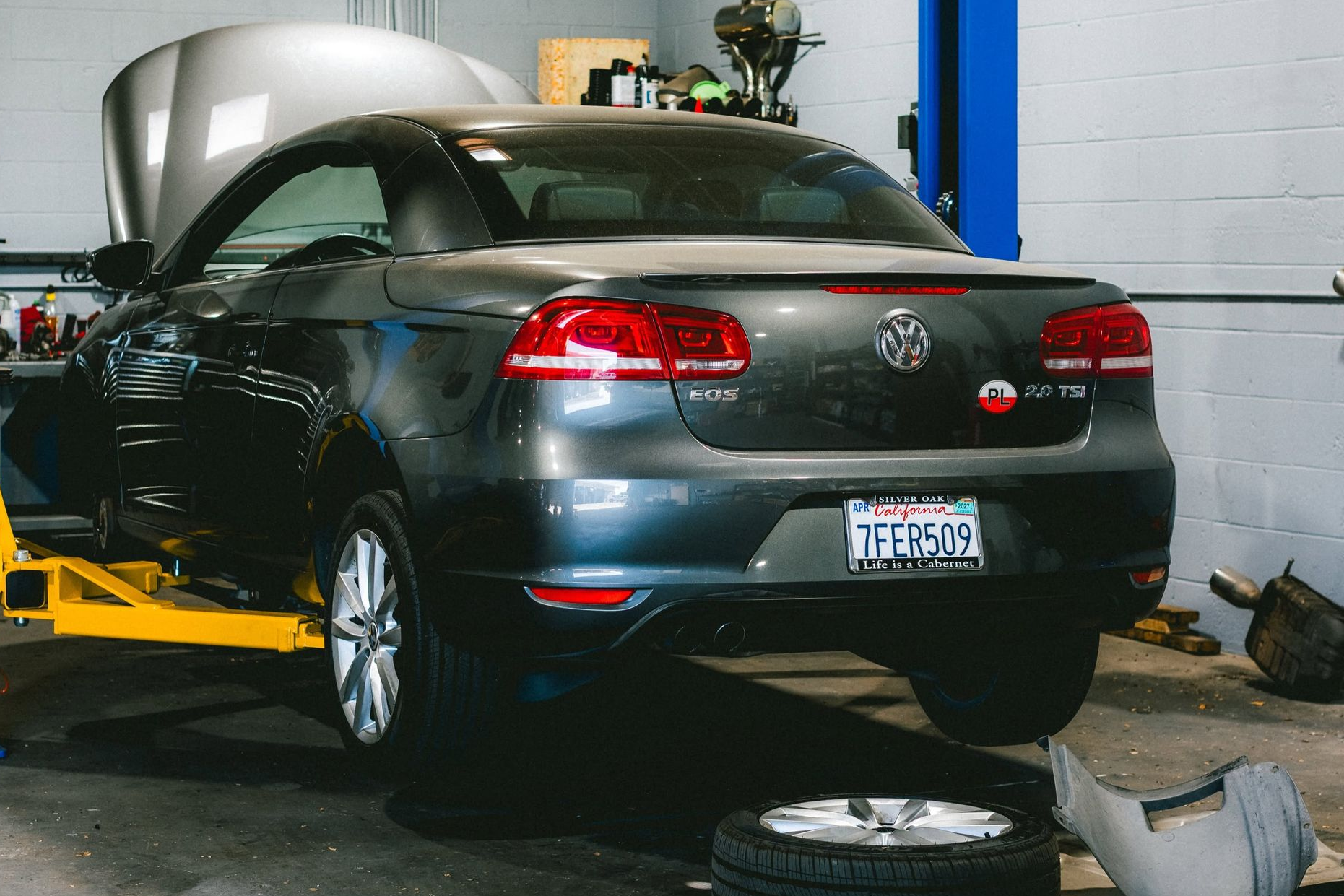 Dark sports car on a lift in a garage, with a spare tire and tools on the floor