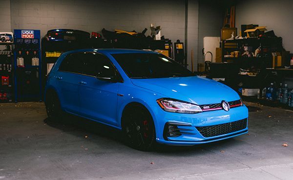 Blue hatchback car parked in a garage with shelves and tools in the background