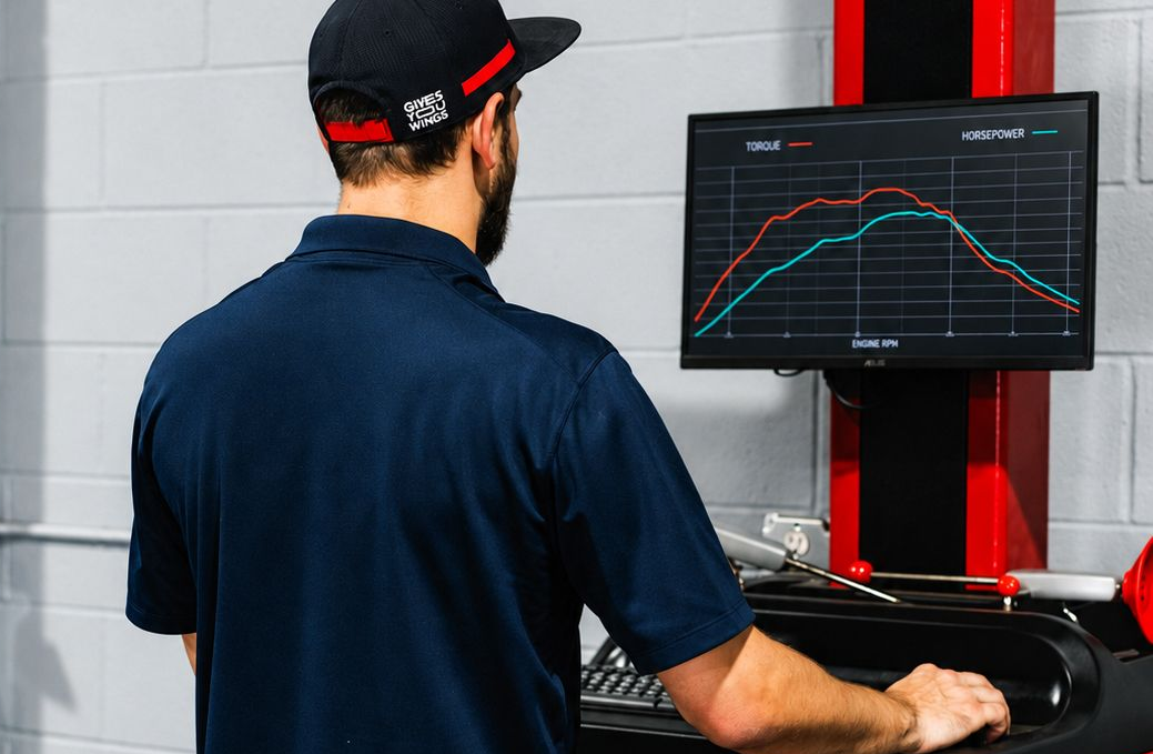 Person operating a machine with a computer monitor showing data graphs in a workshop.
