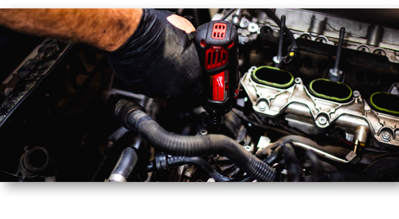 Mechanic using a red power tool in a car engine bay, with green-capped components visible